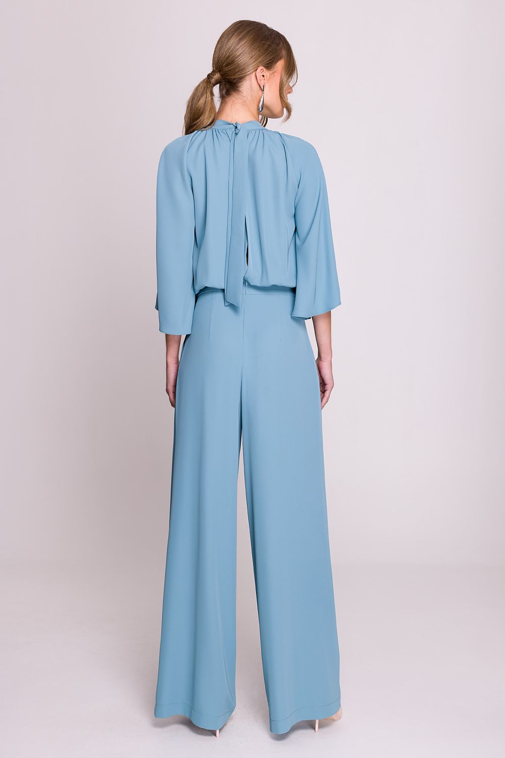 Femme portant un ensemble fluide bleu ciel à manches chauve-souris, pantalon large taille haute, fabriqué en Europe, mode parisienne chic.