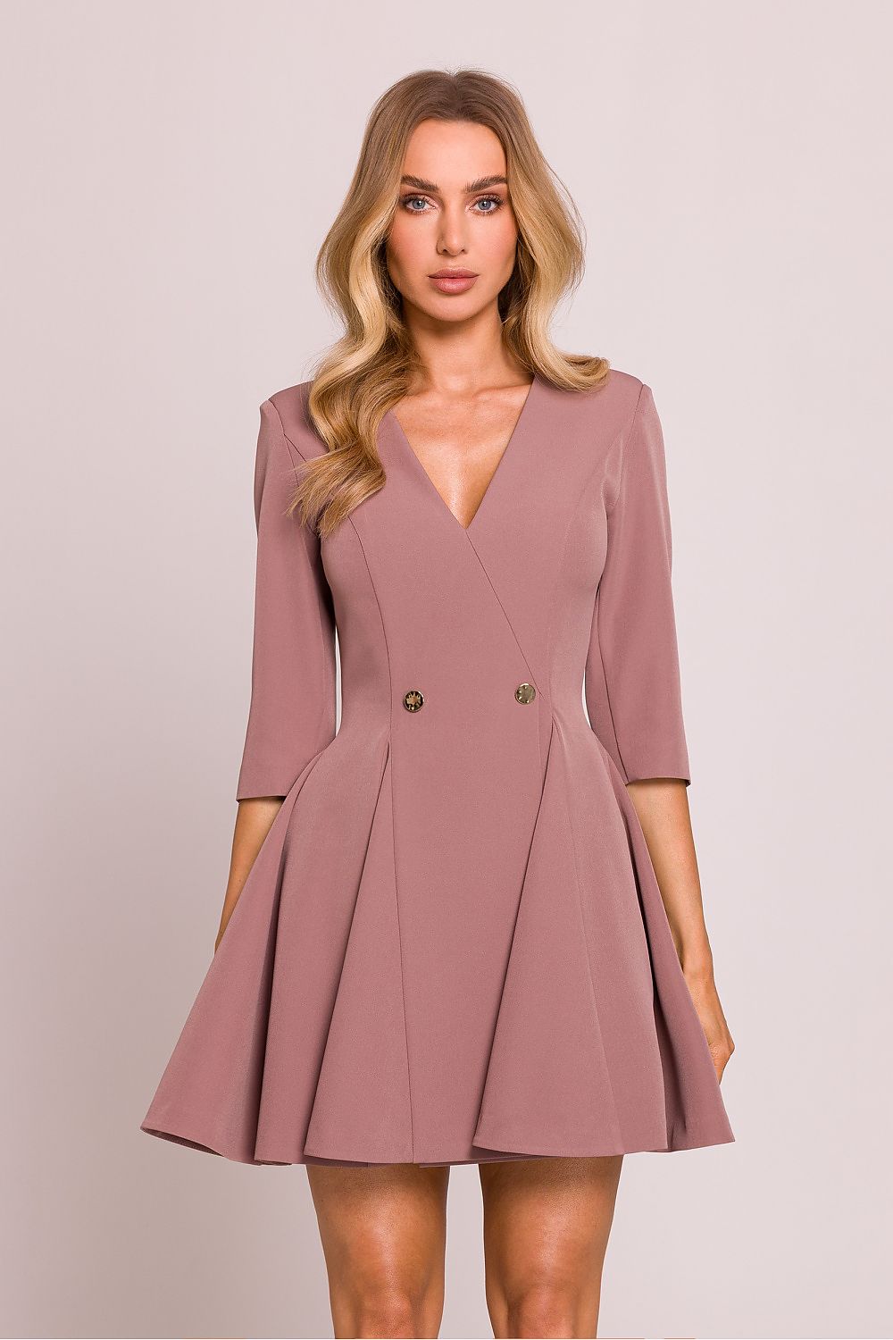 Femme portant une robe courte rose en tissu lisse avec décolleté en V et boutons décoratifs à la taille, coupe évasée élégante, fabriquée en Europe, mode parisienne