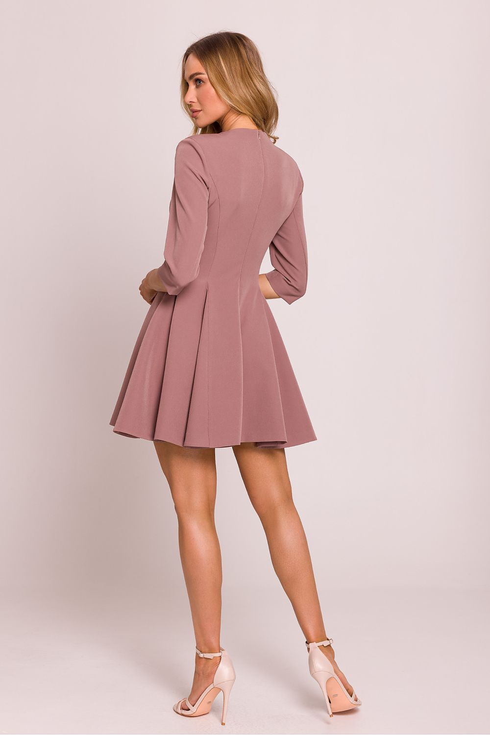 Femme portant une robe courte rose en tissu lisse avec décolleté en V et boutons décoratifs à la taille, coupe évasée élégante, fabriquée en Europe, mode parisienne