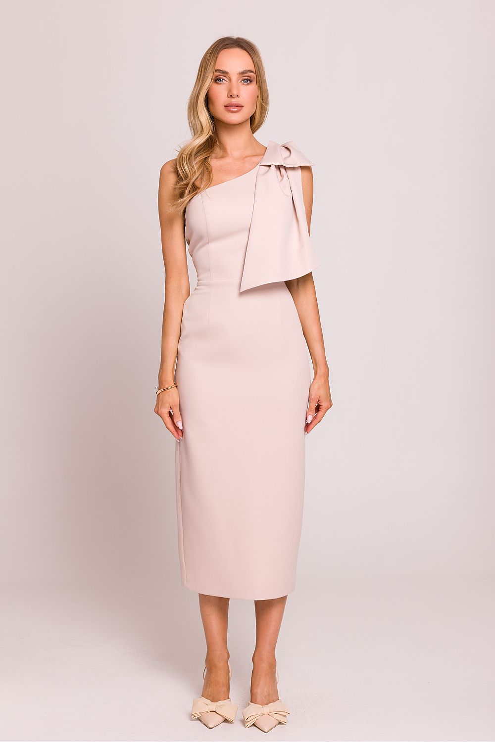 Femme portant une robe midi rose pâle à une épaule avec nœud décoratif, coupe asymétrique et fente arrière, fabriquée en Europe, mode parisienne