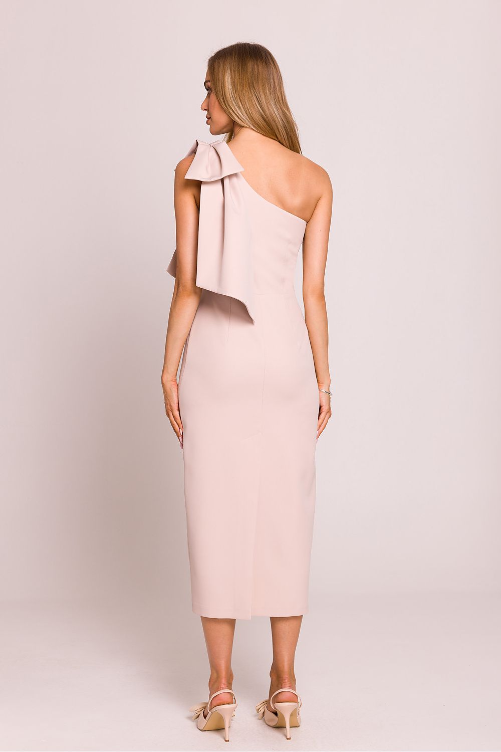 Femme portant une robe midi rose pâle à une épaule avec nœud décoratif, coupe asymétrique et fente arrière, fabriquée en Europe, mode parisienne