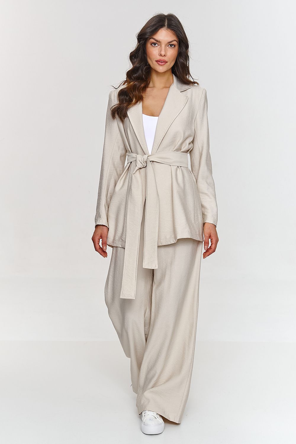 Femme portant un ensemble beige élégant avec blazer ceinturé et pantalon large, fabriqué en Europe, mode parisienne