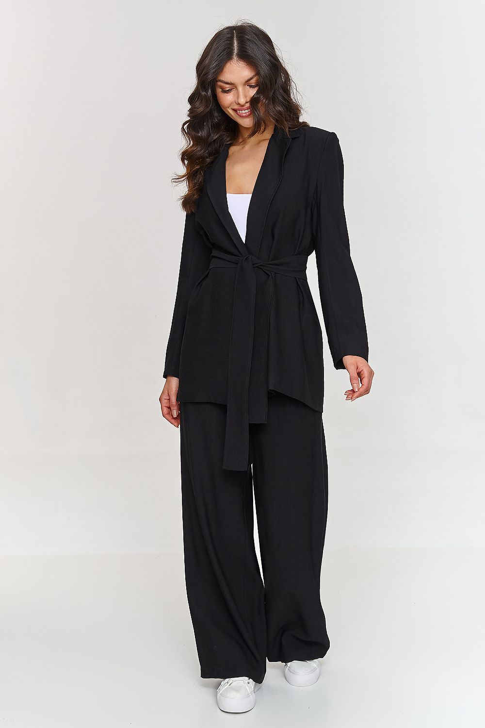 Femme portant un ensemble noir élégant avec blazer ceinturé et pantalon large, fabriqué en Europe, mode parisienne
