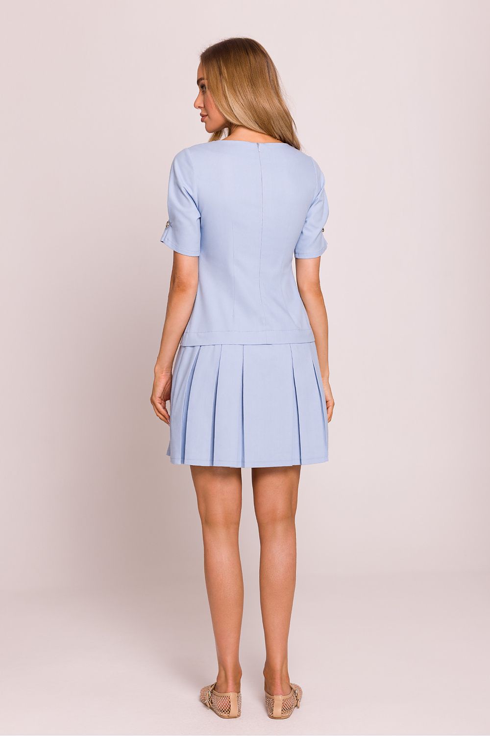 Femme portant une robe mini bleu clair en coton à taille basse, manches courtes et détails boutons, fabriquée en Europe, mode parisienne