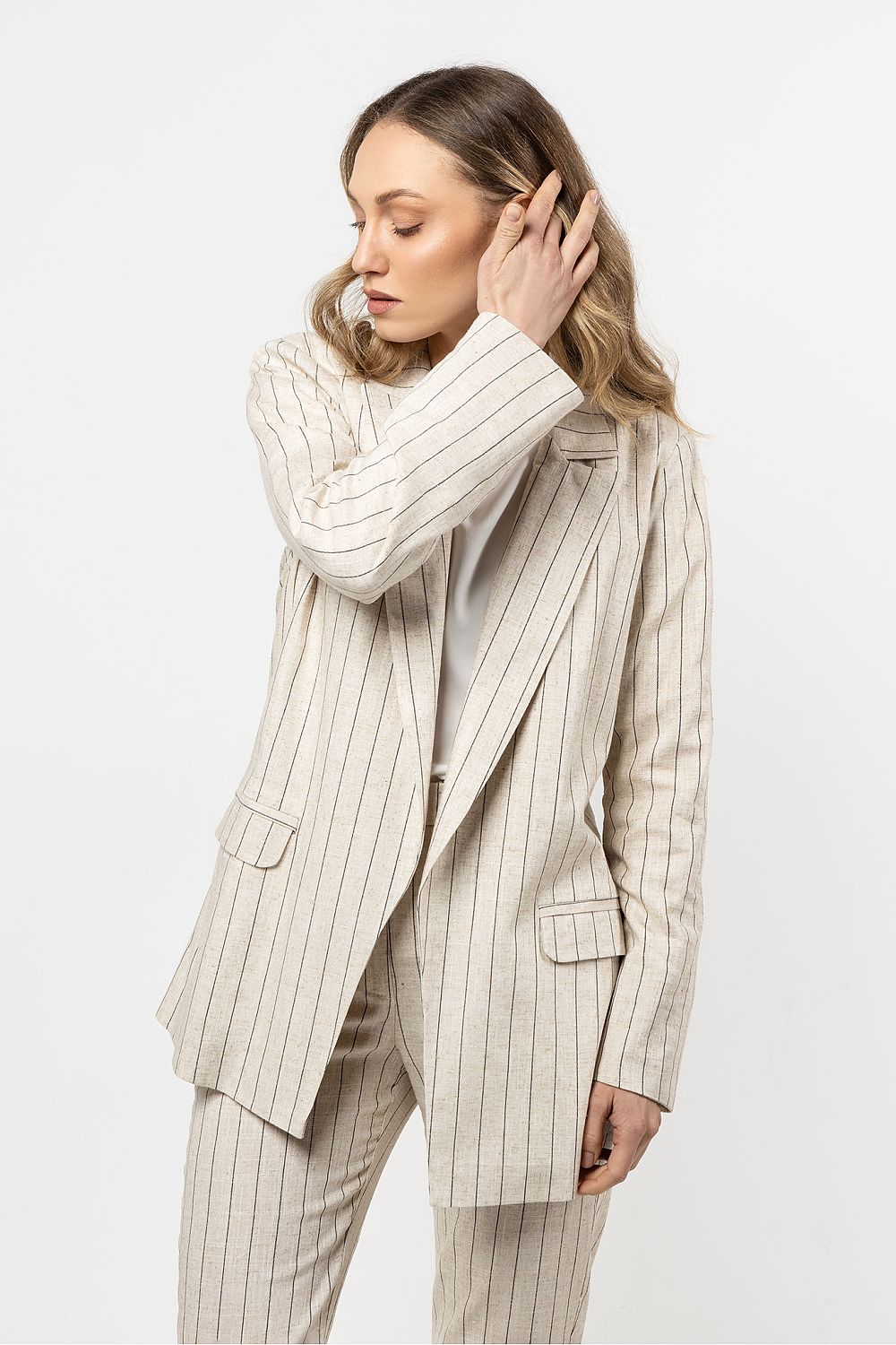 Femme portant une veste en lin beige clair à rayures fines, au style chic et décontracté.