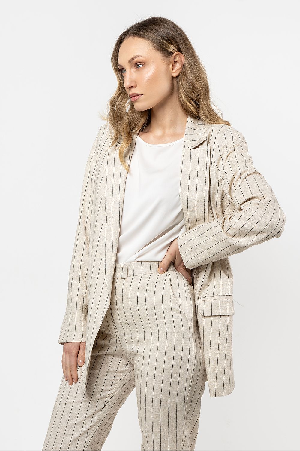 Femme portant une veste en lin beige clair à rayures fines, au style chic et décontracté.