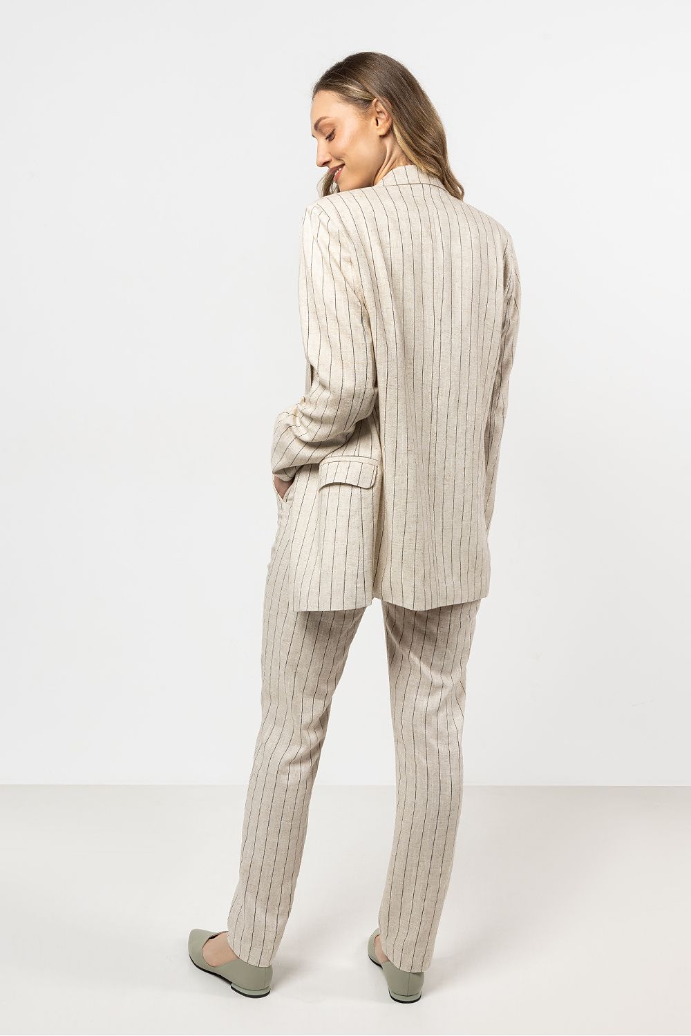 Femme portant une veste en lin beige clair à rayures fines, au style chic et décontracté.