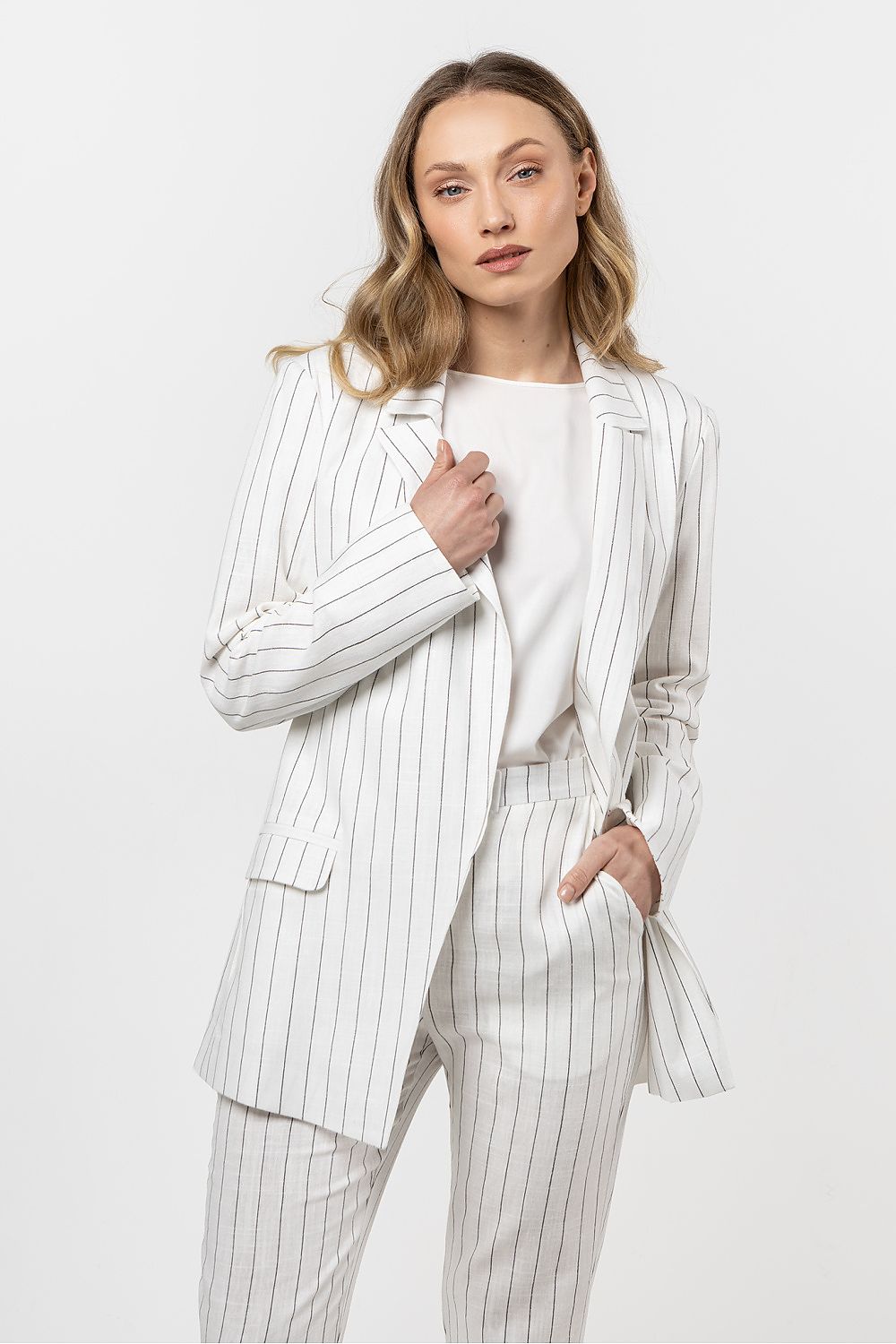 Femme portant une veste en lin blanc à rayures discrètes, coupe fluide et sophistiquée.