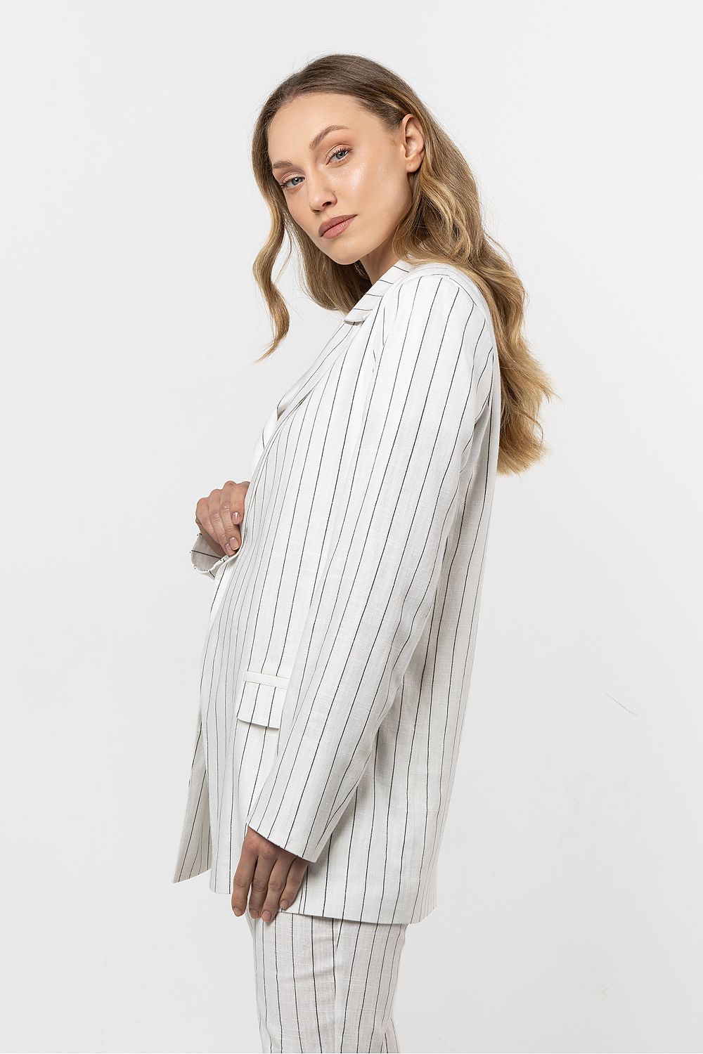Femme portant une veste en lin blanc à rayures discrètes, coupe fluide et sophistiquée.