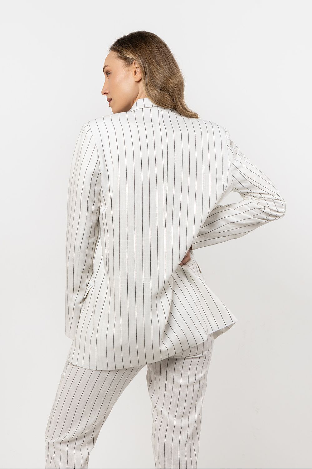 Femme portant une veste en lin blanc à rayures discrètes, coupe fluide et sophistiquée.