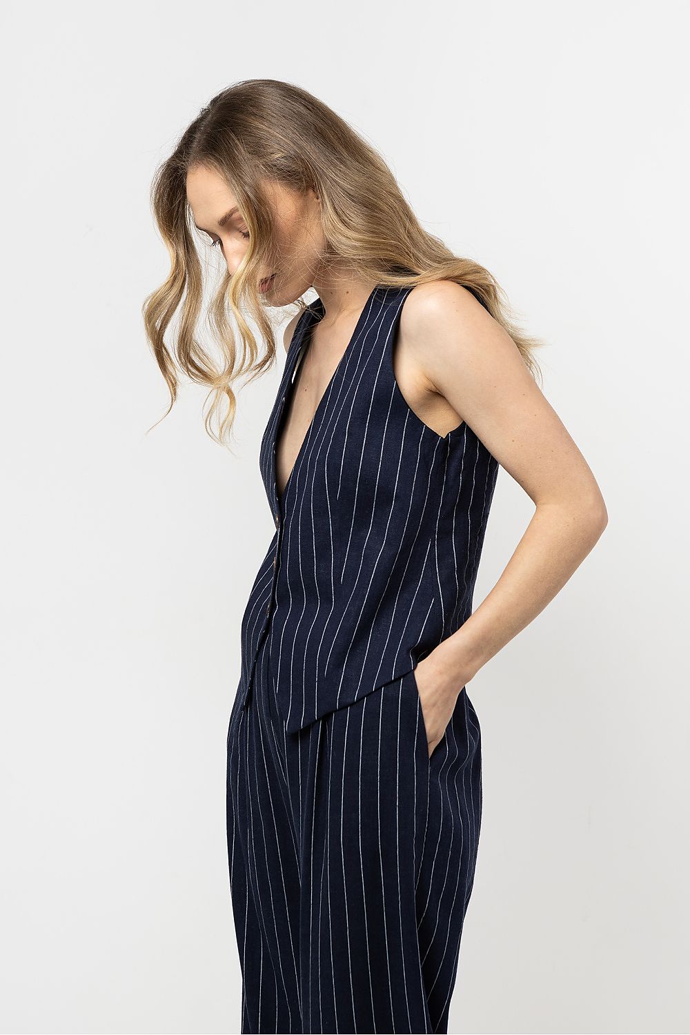 Femme portant un gilet sans manches en lin bleu marine à rayures fines, coupe courte élégante.