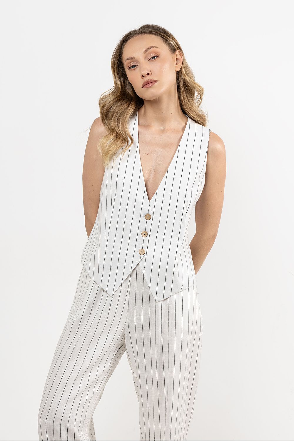 Femme portant un gilet sans manches en lin blanc, coupe droite et col en V sophistiqué.