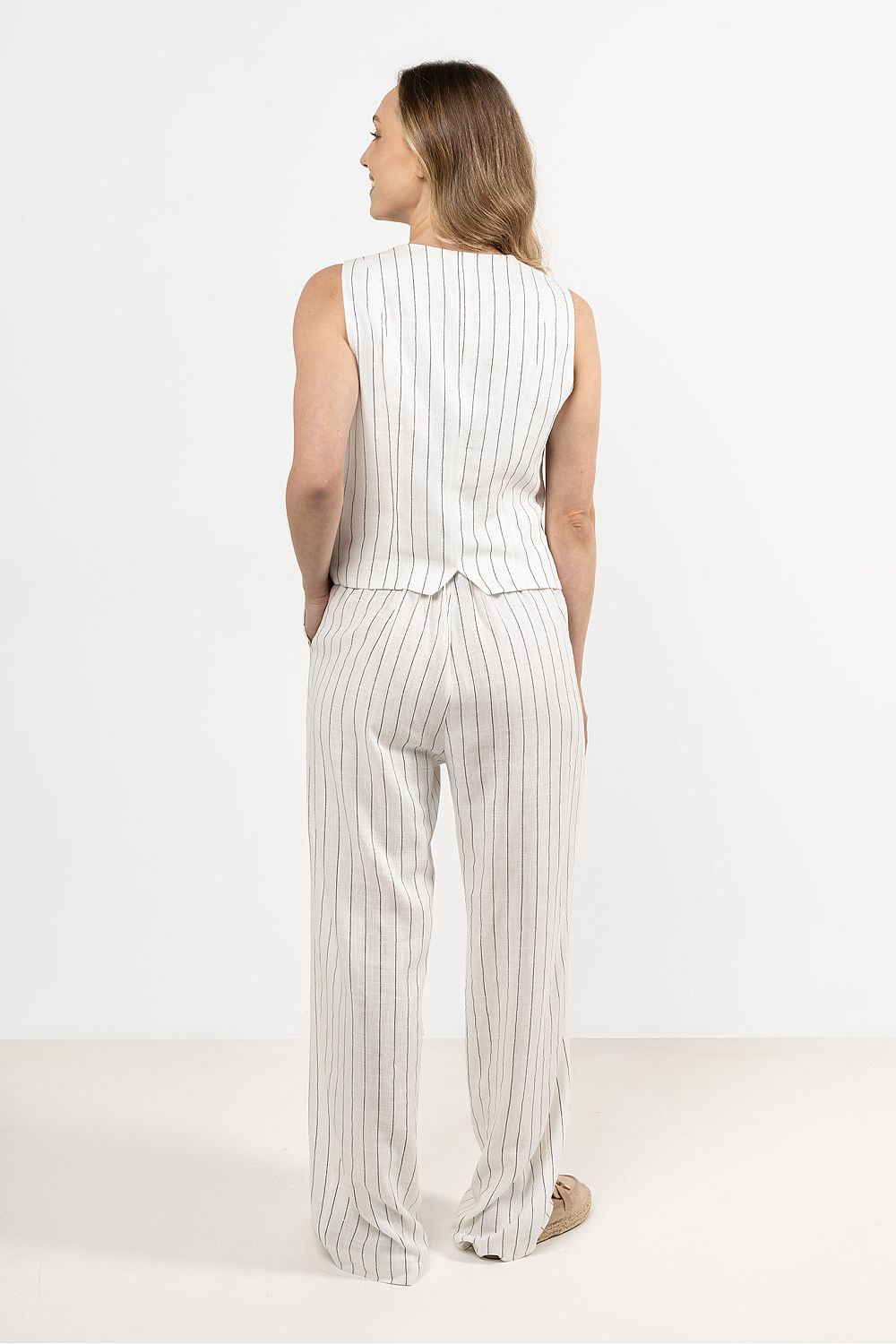 Femme portant un gilet sans manches en lin blanc, coupe droite et col en V sophistiqué.