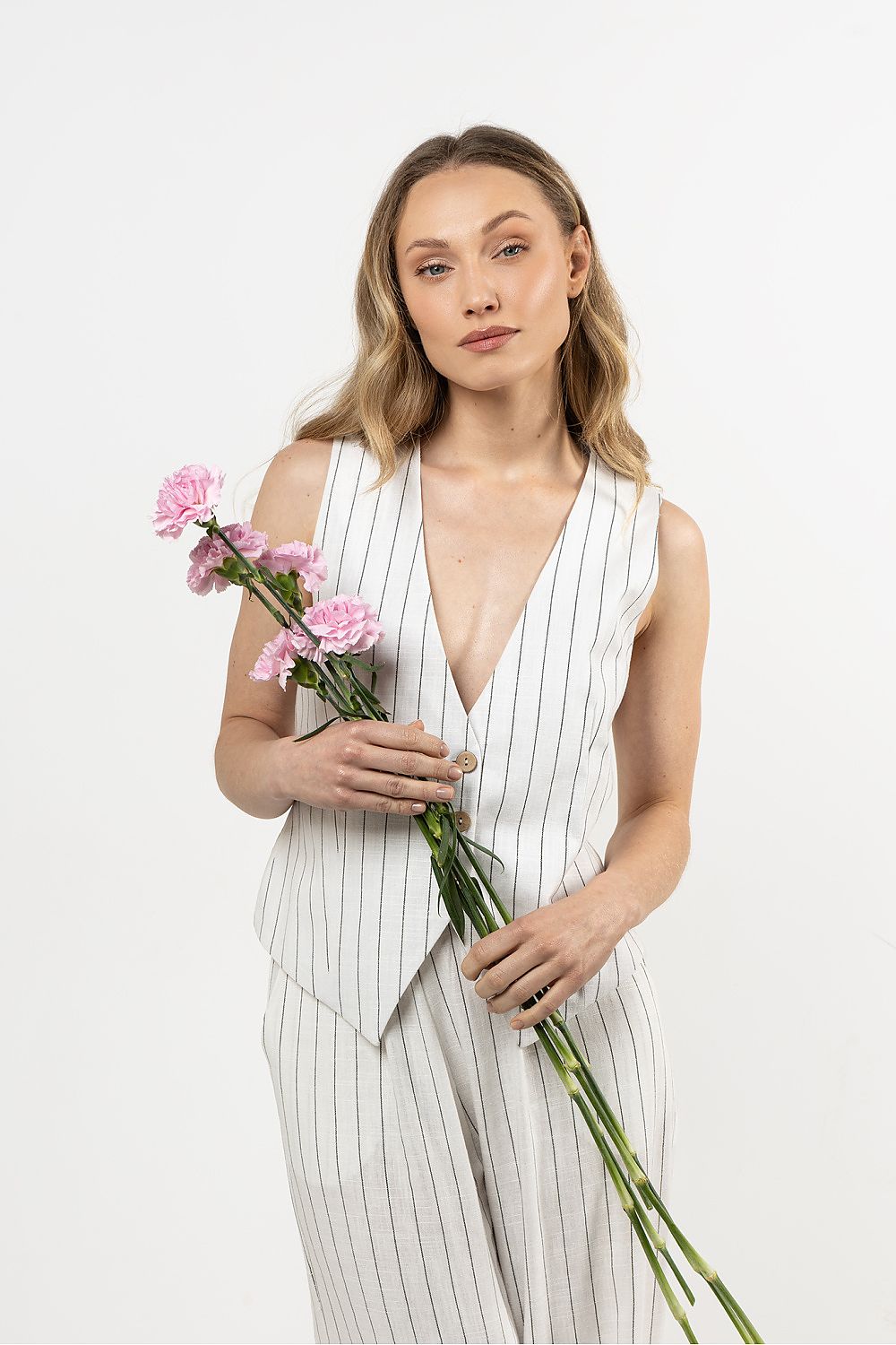 Femme portant un gilet sans manches en lin blanc, coupe droite et col en V sophistiqué.