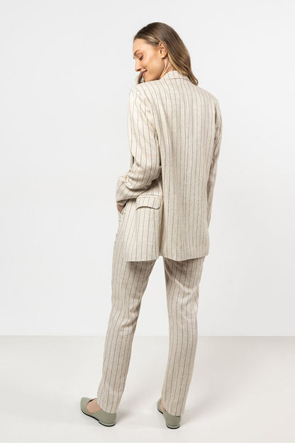 Femme portant une veste en lin beige clair à rayures fines, au style chic et décontracté.