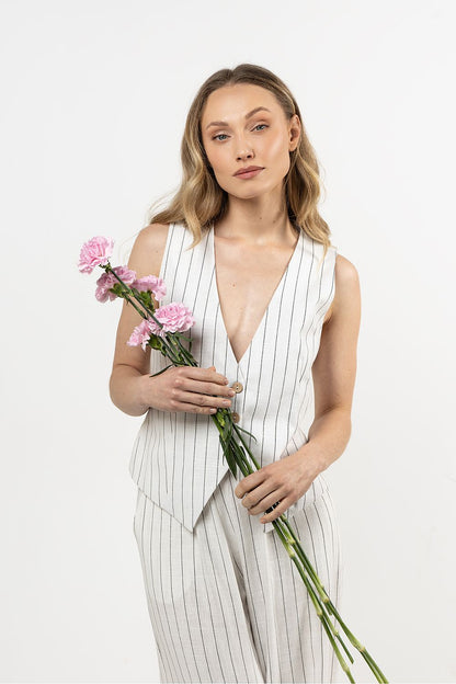 Femme portant un gilet sans manches en lin blanc, coupe droite et col en V sophistiqué.